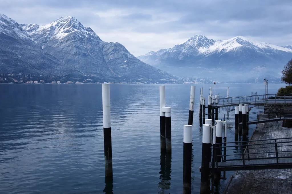 Téli látkép a Comói-tóról: hófödte hegyek, csendes tófelszín és egy kikötő a parton, amely jól mutatja, milyen a Comói-tó télen